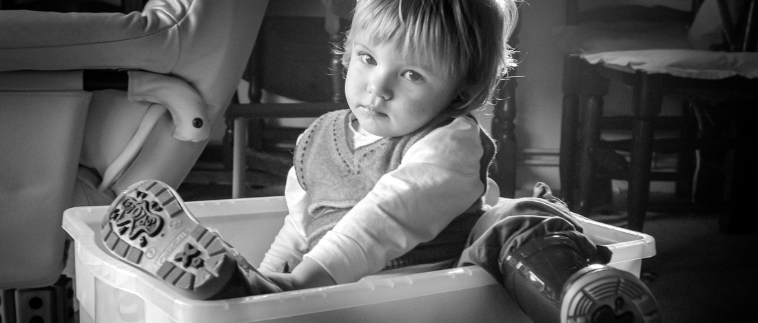 Black and white photograph of bored toddler sitting in a toy box
